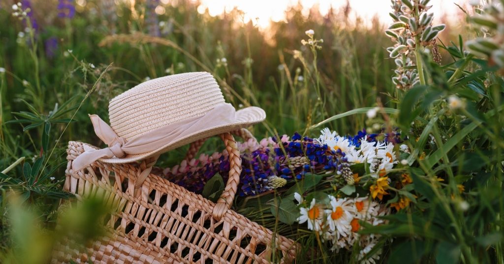 beautiful bouquet of lupines lies in a bag together with a straw hat on the grass in the field. Horizontal shot